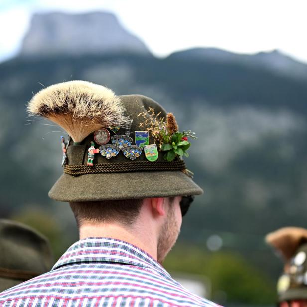 Ein Mann mit Hut mit Gamsbart und Ansteckern vor Bergkulisse